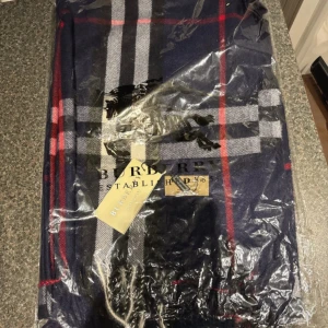 Rutig halsduk från Burberry i ull - Snygg rutig halsduk från Burberry i marinblått med röda, vita och grå ränder. Tillverkad i 100% ull och har den klassiska Burberry-looken. Perfekt accessoar för att lyfta din outfit med en tidlös touch.