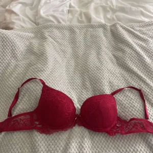 Röd spets-bh från Censored 80D - Snygg röd bh från Censored i storlek 80D. Bh:n har vadderade kupor och vackra spetsdetaljer längs kanterna och banden. Axelbanden är justerbara och ryggen har klassisk knäppning. Perfekt för dig som vill ha något extra fint under.