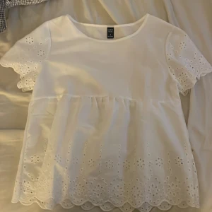 Vit blus  - Superfin vit blus från shein med korta ärmar och broderade blommor samt hålbroderier längs ärmar och nederkant. Blusen har en lös passform och volangliknande avslut nertill. Perfekt för en fräsch och söt look i sommar eller vår.