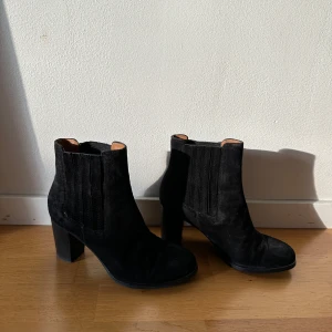 Svarta mocka chelsea boots med klack - Snygga svarta chelsea boots i mocka från & Other Stories. Skorna har bred resår på sidorna, rund tå och stabil hög klack. Perfekta för dig som vill ha en stilren och tidlös look med lite edge.