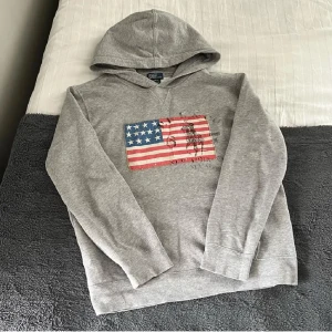 Ralph Lauren USA Flag Hoodie - Säljer denna tvärfeta och sällsynta Ralph Lauren Hoodien. Storlek L (14-16) men sitter lite större och passar en XS eller mindre S. Fint skick. Hör gärna av er vid funderingar🙌
