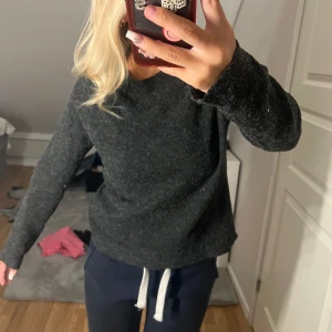 Mörkgrå stickad tröja med rund hals - Mysig mörkgrå stickad tröja med rund hals och långa ärmar. Tröjan har en enkel och clean look, perfekt att slänga på sig när det är lite kyligt. Materialet är mjukt och känns skönt mot huden. Passformen är normal och den är lätt att matcha med jeans eller mjukis.