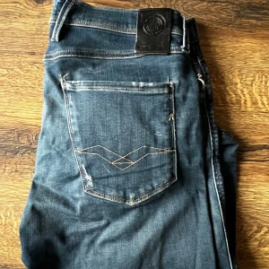 Replay hyperflex ambass - Säljer ett par blå jeans från Replay med snyggt slitna detaljer och klassisk femficksdesign. Jeansen har smal passform och normal midja, med coola kontrastsömmar på bakfickan. Perfekta för dig som gillar en modern och avslappnad stil.