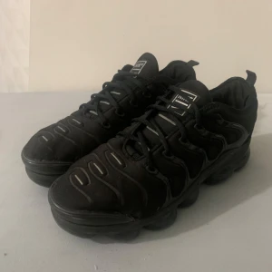 Svarta Nike sneakers med unik sula - Svarta Nike sneakers med cool, vågig design och robust, mönstrad sula. Skorna har snörning och diskreta logodetaljer på plösen och hälen. Tillverkade i syntetmaterial och textil, perfekta för dig som gillar sportig och urban stil.