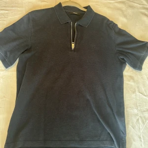 Mörkblå pikétröja Jack & Jones  - Snygg mörkblå pikétröja från Jack & Jones Premium i storlek S. Täcken på användning. Tröjan har klassisk krage, korta ärmar och en cool dragkedja framtill istället för knappar. Materialet känns mjukt och bekvämt, perfekt för en stilren look.