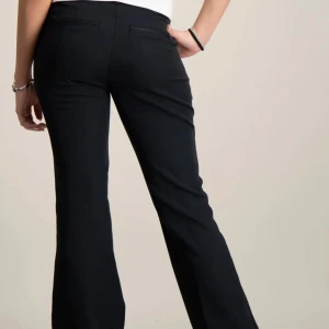 Svarta bootcut kostymbyxor - Snygga svarta kostymbyxor med bootcut passform och klassiska fickor bak. Byxorna har en stilren look och är perfekta för dig som gillar en tidlös och trendig stil. Materialet är mjukt och följsamt för en bekväm känsla hela dagen.