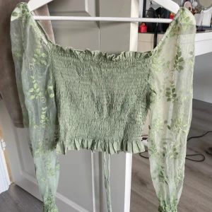Grön blus med meshärmar från SHEIN - Supersöt ljusgrön blus från SHEIN med smockad kropp och volangkant nertill. Långa transparenta meshärmar med broderade blommor och resår vid handlederna. Offshoulder-modell som ger en romantisk vibe. Perfekt för vår och sommar!