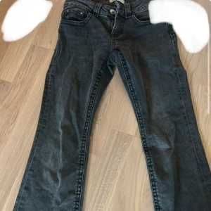 Mörkblå bootcut jeans med fickdetaljer - Snygga mörkblå jeans med bootcut passform och coola fickor med knappar bak. Klassisk femficksmodell och dragkedja framtill. Perfekta för dig som gillar en lite vidare siluett nertill och vill ha en tidlös look.