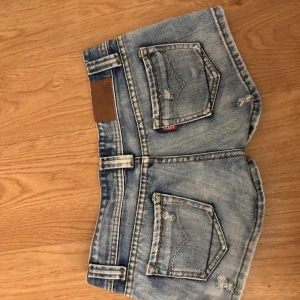 Levi's ljusblå jeansshorts low waisted - Snygga ljusblå jeansshorts från Levi's med coola slitningar och klassiska fem fickor. Shortsen har normal passform, midwaist och detaljer som knapp och dragkedja framtill. Perfekta för sommarens alla äventyr och har en fräsch tvättad look. från spanien 