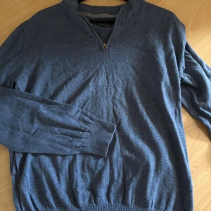 Blå stickad tröja med half zip  - Snygg blå stickad tröja från Riley i storlek XXL. Tröjan har en stilren half zip-dragkedja vid halsen och ribbade muddar vid ärmslut och nederkant. Perfekt för dig som gillar en klassisk look med modern touch.