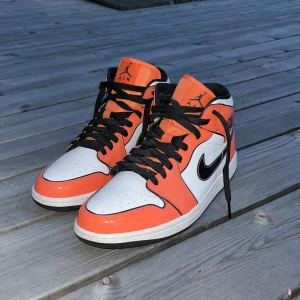 Nike Air Jordan 1 Mid orange/vit - Säljer ett par Nike Air Jordan 1 Mid i orange och vitt med svarta detaljer och svart swoosh. Skorna har klassisk snörning, svart yttersula och hög siluett. Perfekta för dig som vill sticka ut med en färgstark sneaker. Modellnummer DD6834-802. (Använda i få tillfällen, kommer även med creaseskydd) 