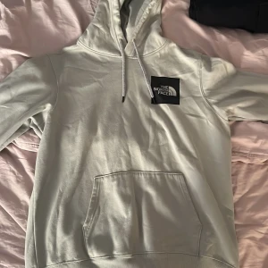 Ljusturkos hoodie från The North Face - Säljer en ljusturkos hoodie från The North Face i storlek L. Tröjan har huva med snörning, stor magficka och en svart patch med logga på bröstet.