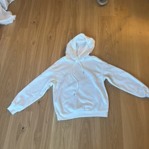 Vit hoodie med tryck 'Rock the world' - Snygg vit hoodie i storlek XS med coolt svartvitt tryck på ryggen som visar två händer med smycken och texten 'Rock the world'. Tröjan har huva med snörning och är långärmad. Aldrig använd!! Pris kan diskuteras!