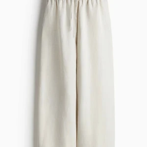 Beiga vida linnebyxor med snörning - Säljer ett par ljusbeiga linnebyxor med bred passform och resår i midjan samt snörning. Byxorna har råa kanter nertill för en chill vibe och är perfekta för varma dagar. Luftiga och sköna i tunt linnetyg.