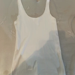 Vit ärmlös linnetopp - En stilren vit linnetopp med rundad halsringning och ärmlös design. Perfekt att matcha med jeans eller kjol för en clean och fräsch look. Enkel och tidlös modell som passar till många olika outfits.