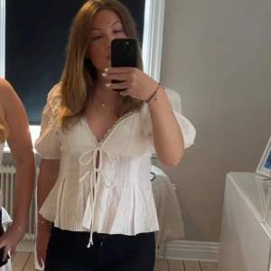 Vit blus med puffärm från NA-KD - Supersöt vit blus från NA-KD med puffiga korta ärmar, v-ringning och två knytband framtill. Blusen har diskret randigt strukturmönster och spetsdetalj längs urringningen. Blusen är använd 2 gånger🩷