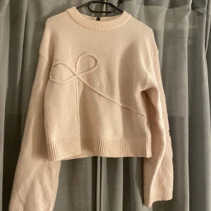 Beige stickad tröja från Divided - Säljer en söt stickad tröja från hm. Tröjan har en unik detalj med en stickad rosett på framsidan och ribbade kanter vid ärmslut och nederkant. Perfekt för kyliga dagar! Den va ljusrosa i början men missfärgades lite i tvätten. Bra skick förutom missfärgningen. Nypris: 299