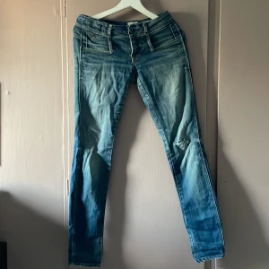 G-Star Cube Skinny jeans blå, strl 26/30 - Säljer ett par G-Star Cube Skinny jeans i blå tvätt med slitningar och snyggt slitna detaljer. Modellen är skinny fit med låg midja och klassiska bakfickor samt bälte bak. Perfekta för dig som gillar en smal siluett och streetig look.