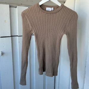 Beige ribbad stickad tröja från Vila - Säljer en beige stickad tröja från Vila i storlek S. Tröjan har ett ribbat mönster och är långärmad med rund hals. Den är slim i passformen och passar perfekt till jeans eller kjol. 