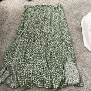 Grön blommig långkjol från H&M 38 - Supersöt grön långkjol från H&M strl 38 med vitt blommigt mönster. Kjolen har en flowy passform och är perfekt för dig som gillar en chill och feminin stil. Lätt material som känns skönt mot huden och passar perfekt till sneakers eller sandaler. 