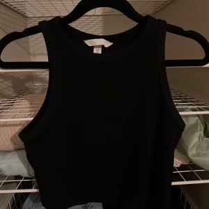 Svart topp - Snygg svart topp som är perfekt för sommaren. Den är ärmlös och croppad, vilket ger en trendig look. Passar utmärkt till både jeans och kjol. 