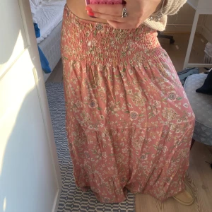 Rosa blommig långkjol - Säljer en superfin rosa långkjol med blommigt mönster. Kjolen har en smockad midja som ger en bekväm passform och ett luftigt fall. Den är one size och passar mig som är vanligtvis en storlek S.💗