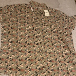 Blommig skjorta från Dressmann - Säljer en blommig skjorta från Dressmann i en skön linneblandning. Skjortan har korta ärmar och ett färgglatt mönster med blommor i olika nyanser. Perfekt för varma dagar!