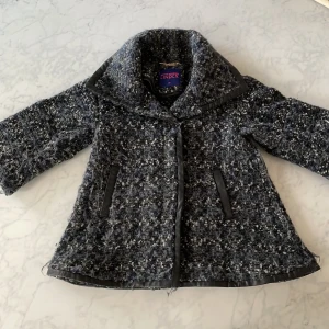 Grå kappa från Matthew Williamson för Lindex - Säljer en elegant grå kappa från Matthew Williamson för Lindex. Den har ett stilrent mönster och är dekorerad med svarta detaljer. Perfekt med sin klassiska design och bekväma passform.