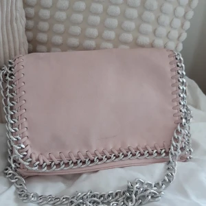 Rosa axelväska med kedjedetaljer - Snygg rosa axelväska med silverfärgad kedja som axelrem och dekorativ kant. Väskan har en dragkedja på baksidan för extra förvaring. Perfekt för att ge en stilren touch till din outfit!💕💕