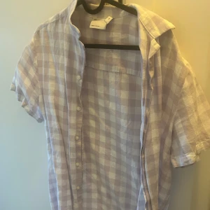 Ljuslila och vit rutig skjorta - Säljer en stilren ljuslila och vit rutig skjorta från COS. Skjortan har korta ärmar och knappar framtill. Perfekt för en avslappnad och trendig look. 🟣