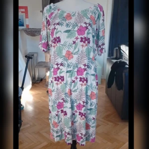 Blommig klänning från Mywear Woman - Charmig blommig klänning från Mywear Woman i storlek S. Klänningen har ett färgglatt mönster med rosa, lila och orange blommor på en beige bakgrund. Den har korta ärmar och en bekväm passform, perfekt för sommarens varma dagar.