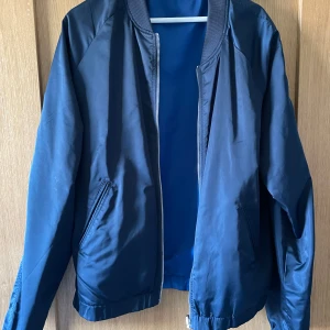 Blå bomberjacka Elvine - Snygg blå bomberjacka med dragkedja och ribbade muddar. Jackan har en klassisk design med två fickor framtill och en bekväm passform. Perfekt för en stilren look.