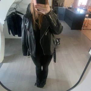 Svart skinnjacka från ONLY - Snygg svart skinnjacka från ONLY med dragkedja och bälte. Perfekt för en cool look. Jackan har långa ärmar och en klassisk bikerstil. Använt typ 3 gånger 