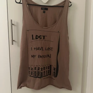 Brun linnetopp med tryck - Säljer en brun linnetopp från Lost med ett unikt tryck på framsidan som säger 'I have lost my passion'. Toppen är ärmlös och har en avslappnad passform. Perfekt för en casual look.