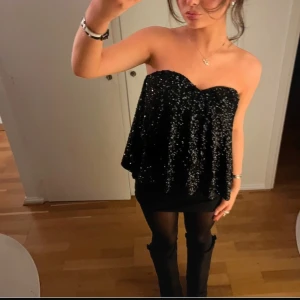 Svart glittrig axelbandslös topp - Snygg svart axelbandslös topp med glittriga detaljer. Perfekt för en kväll ute. Använd en gång!