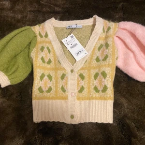 Flerfärgad kofta från Zara - Säljer en unik flerfärgad kofta från Zara med puffiga ärmar i grönt och rosa. Koftan har ett gult och beige mönster med knappar framtill, mjukaste materialet. Sjukt söt. Oanvänd nypris 359:-