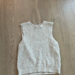 Beige stickad väst - Säljer en stilren beige stickad väst/slipover. Perfekt för lager-på-lager under kyligare dagar. Västen har en klassisk passform och är ärmlös, vilket gör den lätt att matcha med olika outfits.