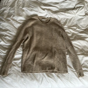 Beige stickad tröja från Acne Studios - Säljer en stilren beige stickad tröja från Acne Studios. Tröjan har en klassisk rund hals och långa ärmar, perfekt för kyligare dagar. Den är mjuk och bekväm, idealisk för både vardag och mer avslappnade tillfällen. Storlek XL, men passar m/mindre L
