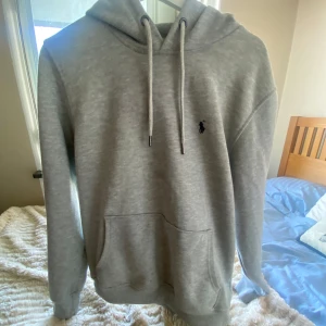 Ralph Lauren hoodie | skriv prisförslag! - Säljer en grå hoodie från Polo Ralph Lauren. Den har en klassisk design med dragsko i huvan och en praktisk magficka. Den har dock ett litet hål som man ser på den sista bilden. Den syns dock knappast när man använder den.