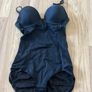 Svart body - Snygg svart body med vadderade kupor och justerbara axelband. Tillverkad i 85% polyamid och 15% elastan för en bekväm passform. Perfekt för uppklätt