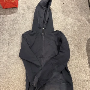 Mörkblå huvtröja från Stone Island - Säljer en snygg mörkblå huvtröja från Stone Island. Tröjan har en dragkedja framtill och en praktisk huva. Perfekt för en avslappnad stil. 🌀 priset går att diskutera! Skicket är bra, däremot ett håll kolla bild 3. Patchen är också spårlöst försvunnen därav pris…(lowkey snyggare utan patch)