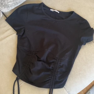 Svart kortärmad topp med snörning - Säljer en stilren svart topp med korta ärmar och snörningsdetalj framtill. Perfekt för en trendig look. Passar bra till både jeans och kjol.