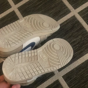 Nike Air Jordans i vitt och blått - Säljer ett par klassiska Nike Air Jordans i vitt med blå detaljer. Skorna har snörning och en rund tå, perfekt för en sportig look. De är tillverkade i syntetmaterial och har den ikoniska Air Jordan-loggan på plösen. Den är bara lite smutsig men inga skador ( crees skydd ingår och pris kan diskuteras ).