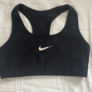 Svart sporttopp från Nike - Säljer en svart sporttopp från Nike med Dri-FIT-teknologi. Toppen har en klassisk design med brottarrygg och är perfekt för träning. Säljer även en i svart och vit mönstrad för 75 och om du är intresserad kan du köpa båda för 100kr