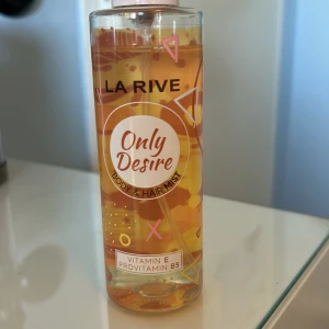 La Rive Only Desire Body & Hair Mist - Fräsch body och hair mist från La Rive med namnet Only Desire. Innehåller vitamin E och provitamin B5 för extra vård. Flaskan är genomskinlig med en färgglad design i orange och rosa toner. Perfekt för att ge både kropp och hår en uppfriskande doft. Använd ett fåtal gånger.