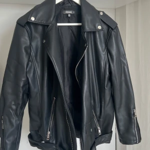 Svart skinnjacka från Missguided - Snygg svart skinnjacka från Missguided med dragkedja och silverfärgade detaljer. Jackan har en klassisk bikerstil med långa ärmar och axelklaffar. Är oversized 