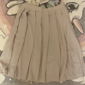 En fin veckad beige kjol - Den har knappt används, kanske 2-3gånger. I väldigt bra skick och har en fin beige färg, kjolen är midi lång. Kedjan funkar som den ska men är lite seg vid toppen. Storlek 38