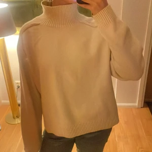 Beige stickad polotröja - Säljer en mysig beige stickad polotröja med ribbade detaljer vid krage, ärmslut och nederkant. Tröjan har en avslappnad passform och långa ärmar. Aldrig använd.