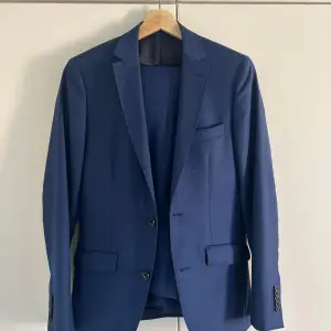 Stilren slim fit kostym av klassiska märket Riley. Köpt från Brothers. Storlek 44 vilket passar dig som en precis runt 170cm. Precis för liten på mig som är 176. Använd ca 3 gånger, finns inget spår av användning. Helt perfekt för skolbalen, fester och evenemang! Kan mötas i Bagarmossen om du vill testa den! Jag säljer även separat en vit skjorta av samma märke och passar dig som bär denna kostym. 