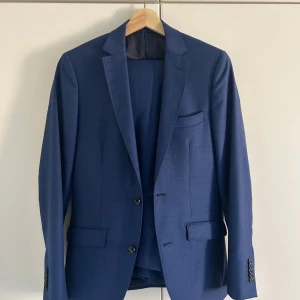 Brothers kostym Riley  - Stilren slim fit kostym av klassiska märket Riley. Köpt från Brothers. Storlek 44 vilket passar dig som en precis runt 170cm. Precis för liten på mig som är 176. Använd ca 3 gånger, finns inget spår av användning. Helt perfekt för skolbalen, fester och evenemang! Kan mötas i Bagarmossen om du vill testa den! Jag säljer även separat en vit skjorta av samma märke och passar dig som bär denna kostym. 